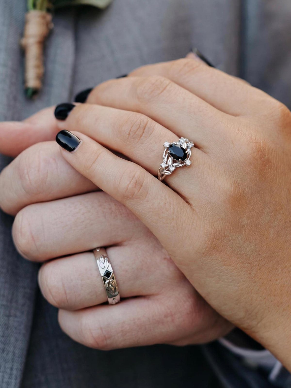 Two hands wearing silver wedding rings layered against a grey suit jacket.