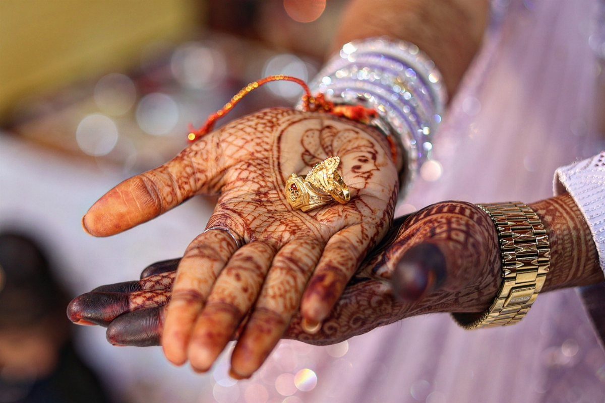 Two gold rings resting on henna-decorated palms with traditional Indian jewelry.