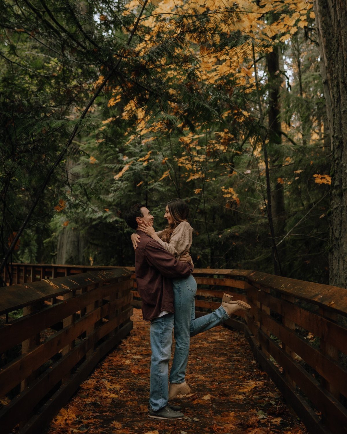 Couple embracing on a wooden bridge wearing burgundy and tan autumn clothing.
