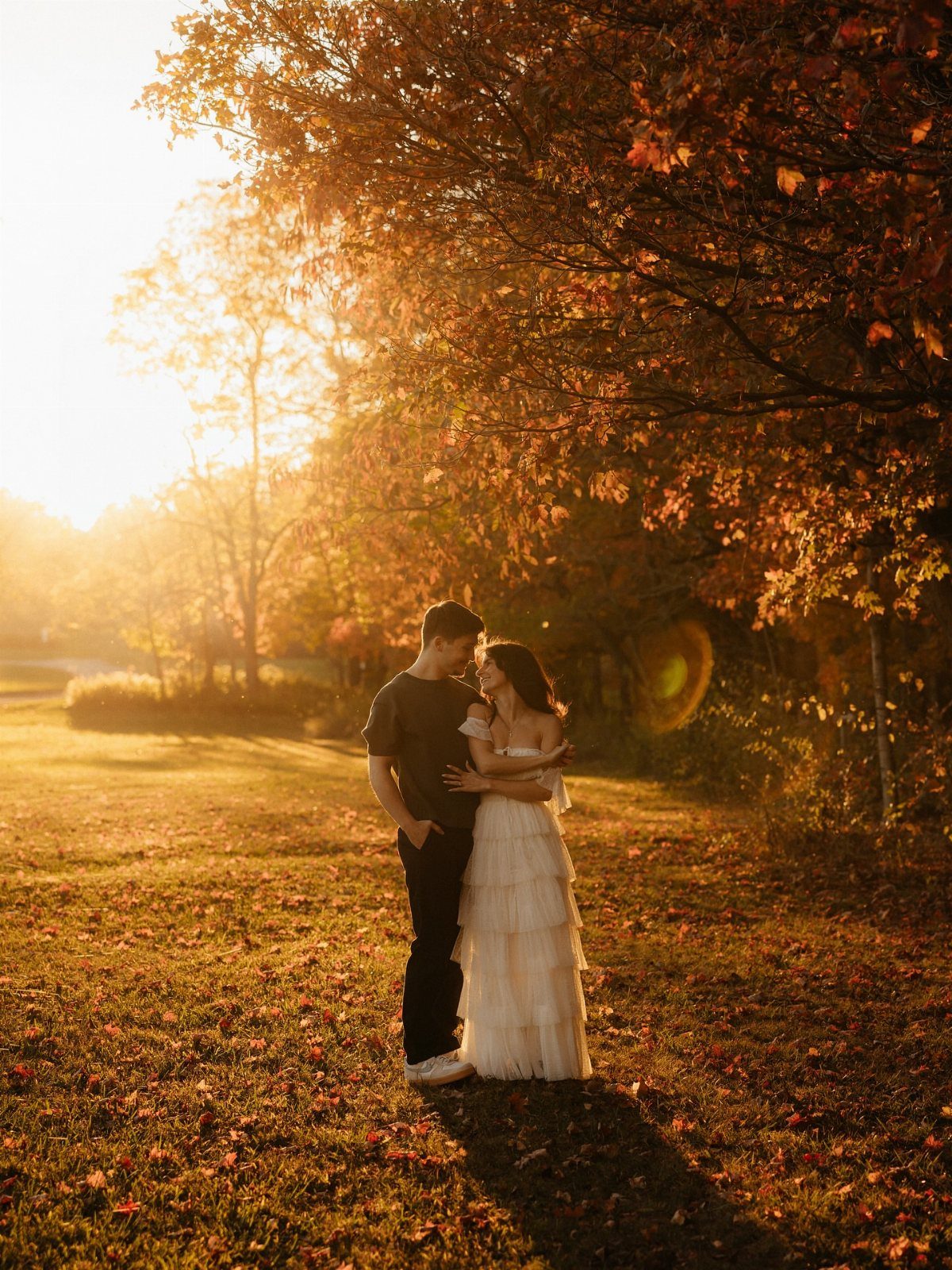 Couple embracing in an autumn field, woman in a tiered white dress.