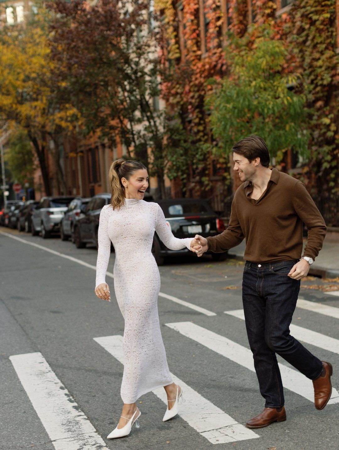 Couple holding hands in a city crosswalk wearing a white lace dress and brown shirt