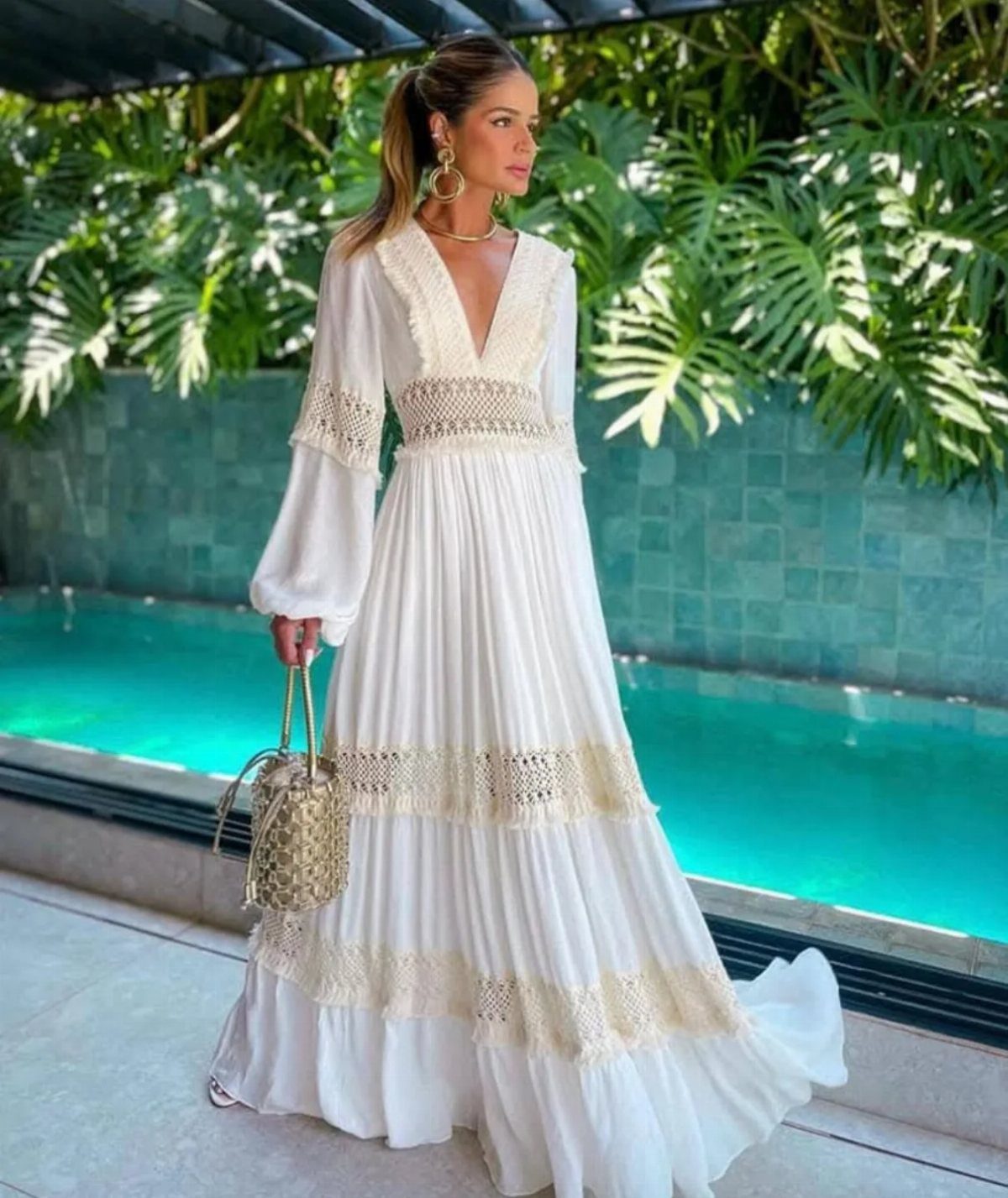 Woman in a long white flowy maxi dress with lace standing by a pool