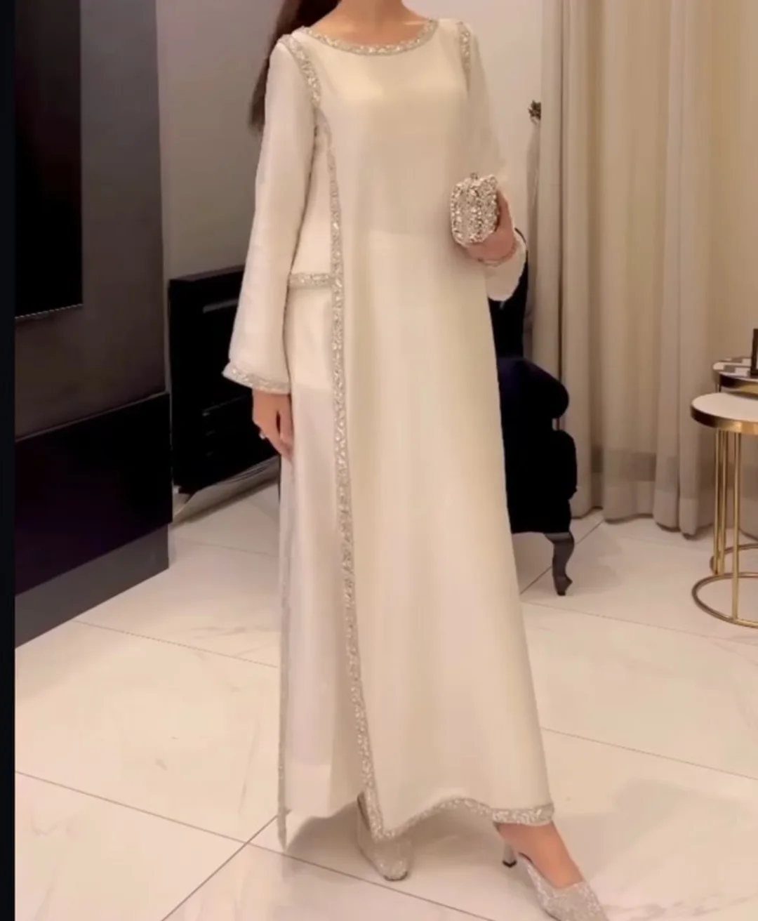 Woman in a long white beaded dress holding a silver clutch indoors